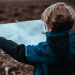 Child in blue jacket holding map outdoors, exploring nature.
