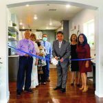 Group cutting a blue ribbon at an indoor event, marking a new opening or celebration.