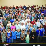 A diverse group of people gathered in a large hall, smiling towards the camera for a group photo.