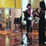 Live band performing with singers and musicians on stage, featuring keyboards and microphones under warm lighting.