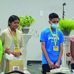 Group of children and adults at an indoor event, wearing badges and masks.