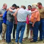 A group of men standing in a circle, participating in a collaborative and supportive group activity outdoors.
