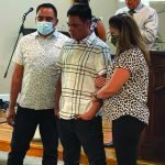 People standing together, heads bowed in prayer at a church service, microphone and podium in background.