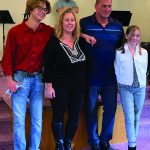 Family posing together indoors with a musician in the background, smiling for the camera.