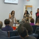 People gathered at a church event, with a woman speaking into a microphone and audience seated attentively.
