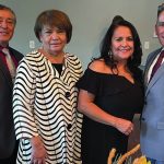 A group of four people dressed formally, smiling at a gathering indoors.