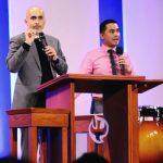 Two speakers at a podium, delivering a presentation in a formal setting.