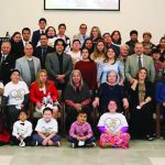 A large group of people gathered for a community event indoors, posing together and smiling for the photo.