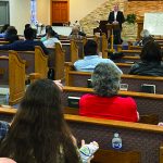 People gathered in a church for a lecture, with a speaker presenting at the front.