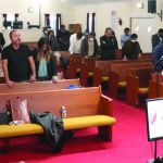 Church congregation praying in pews during service at Iglesia de Dios, pastor speaking from podium.