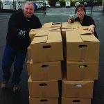Two people stacking cardboard boxes outdoors, preparing for transport.