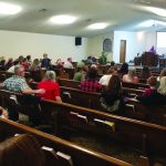 Congregation seated in a church, listening to a speaker at the pulpit during a service or presentation.