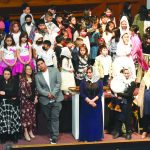 Group of children and adults in diverse attire on stage during a school or community event.