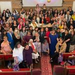 A large group of women gathered in a church setting, posing together for a community event inside a hall.