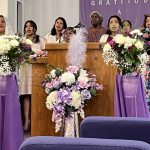 Church choir performing with floral arrangements in purple and white.