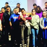 A group of people standing united on a stage in a solemn gathering or ceremony.