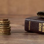 Stack of coins beside a Bible on a wooden table, highlighting the intersection of faith and finance.