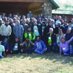 Large group outside a building for a team gathering or event on a sunny day, with some wearing matching green shirts.