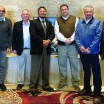 Group of seven men in business attire posing together indoors.