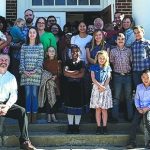 A diverse group of people gathered in front of a building, smiling and posing for a group photo on the steps.