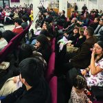 Audience attentively listening at a crowded event in a hall with a speaker on stage.