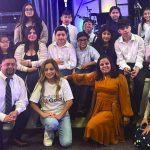 Group of people, including children and adults, posing together indoors at an event.