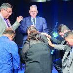 People participating in a prayer ceremony at a church event, with hands placed on shoulders in blessing.