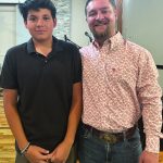 Two people smiling in a room with wooden flooring and a stone accent wall in the background.