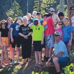 Group of people enjoying a sunny day in a forest setting with trees in the background.