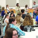 Group of people at a community event with tables, talking and serving food.
