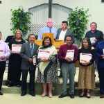 Church graduation ceremony with attendees holding certificates, standing on stage with a podium and crossed symbols behind.