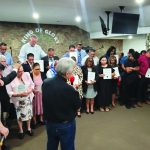 People gathered in a church ceremony, holding certificates, under King of Glory sign.