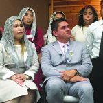 Group of people attending a formal event, with some wearing veils and others in suits and dresses.