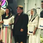 People holding certificates at a ceremony with a speaker in the background.