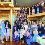 A large group of women in elegant hats gathered indoors, posing on a staircase during a social event.
