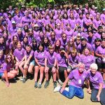 Large group photo of people in matching purple shirts at an outdoor gathering.