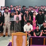 Group of people standing together in a hall, some dressed formally, possibly for a ceremony or event.