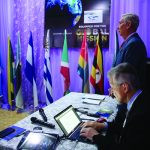 Conference setup with international flags, two men, and a laptop, highlighting a Global Mission theme.