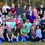 A large group of people posing outdoors in front of a tractor during a family or community gathering.