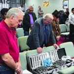 People standing in prayer at a meeting, with audio equipment cases on chairs in the foreground.
