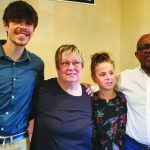 A group of four people standing together indoors, smiling and posing for a photo.