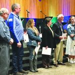 Group of people standing in a row, receiving certificates during an indoor event.