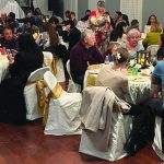 Guests enjoying a lively dinner event with round tables, white tablecloths, and friendly conversations.
