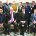 Group of fifteen businessmen in suits gathered for a formal meeting, posing together in a modern office setting.