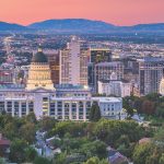 Skyline of Salt Lake City at sunset with the Utah State Capitol and mountains in the background.
