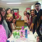 A group of smiling people gathered around a table with crafts and decorations in a bright room.