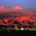 City skyline at dusk with glowing mountains under vibrant sunset sky.
