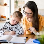 Child learning at home with a woman assisting, engaged in writing at a cozy kitchen table.