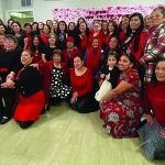 Group of women in red and black attire pose for a photo at a Valentine's themed gathering indoors.