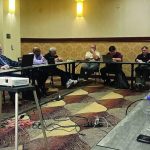 Group meeting in a conference room with people using laptops around a large table.